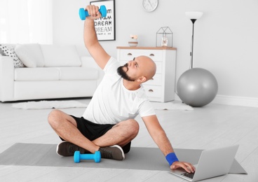 Photo of Overweight man doing exercise while watching tutorial on laptop at home