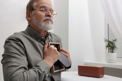 Upset senior man holding photo frame at home. Loneliness concept