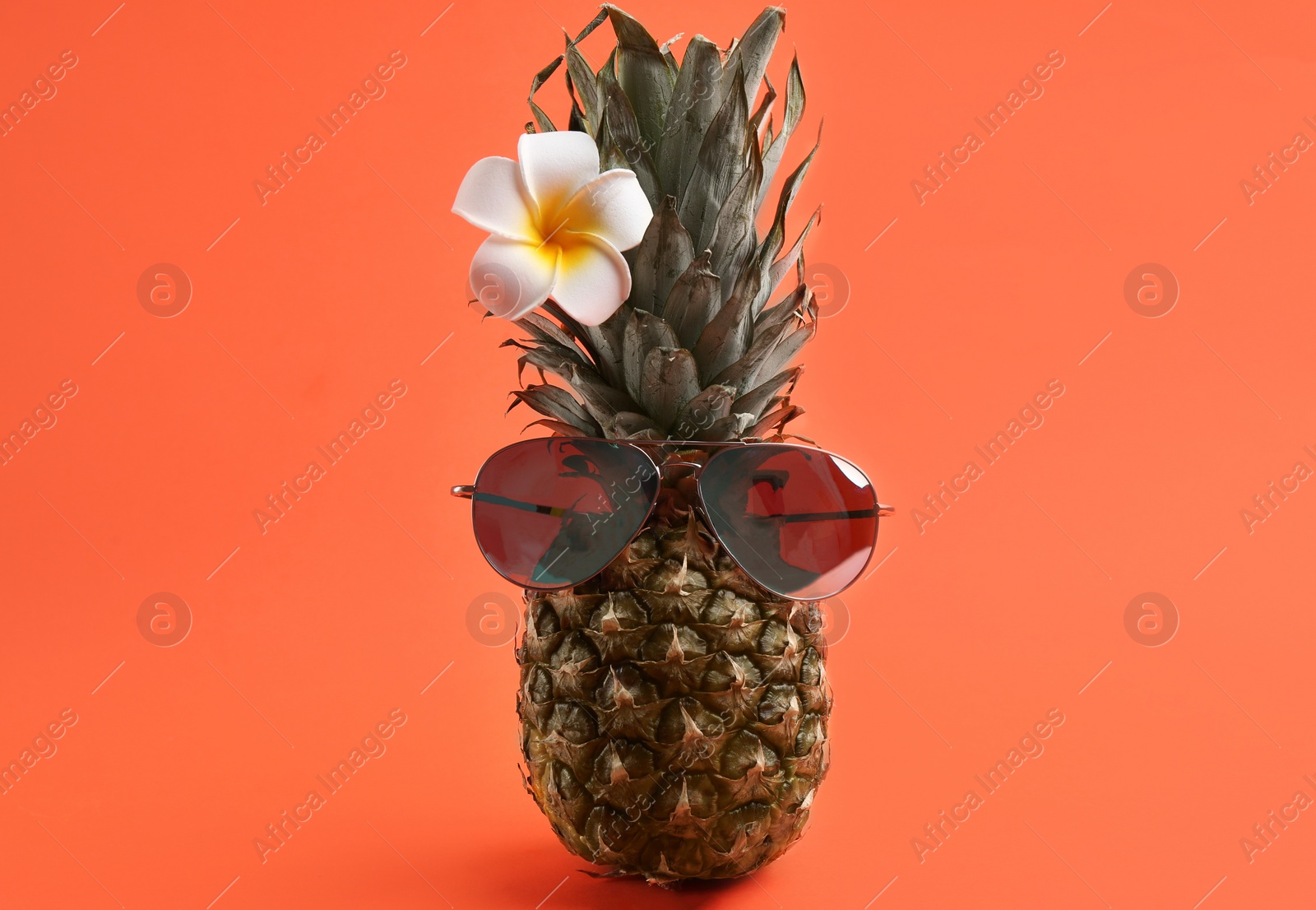 Photo of Funny face made of pineapple with sunglasses and flower on coral background. Vacation time