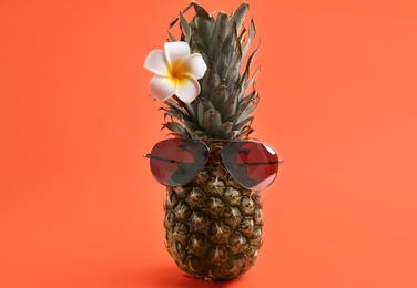 Photo of Funny face made of pineapple with sunglasses and flower on coral background. Vacation time