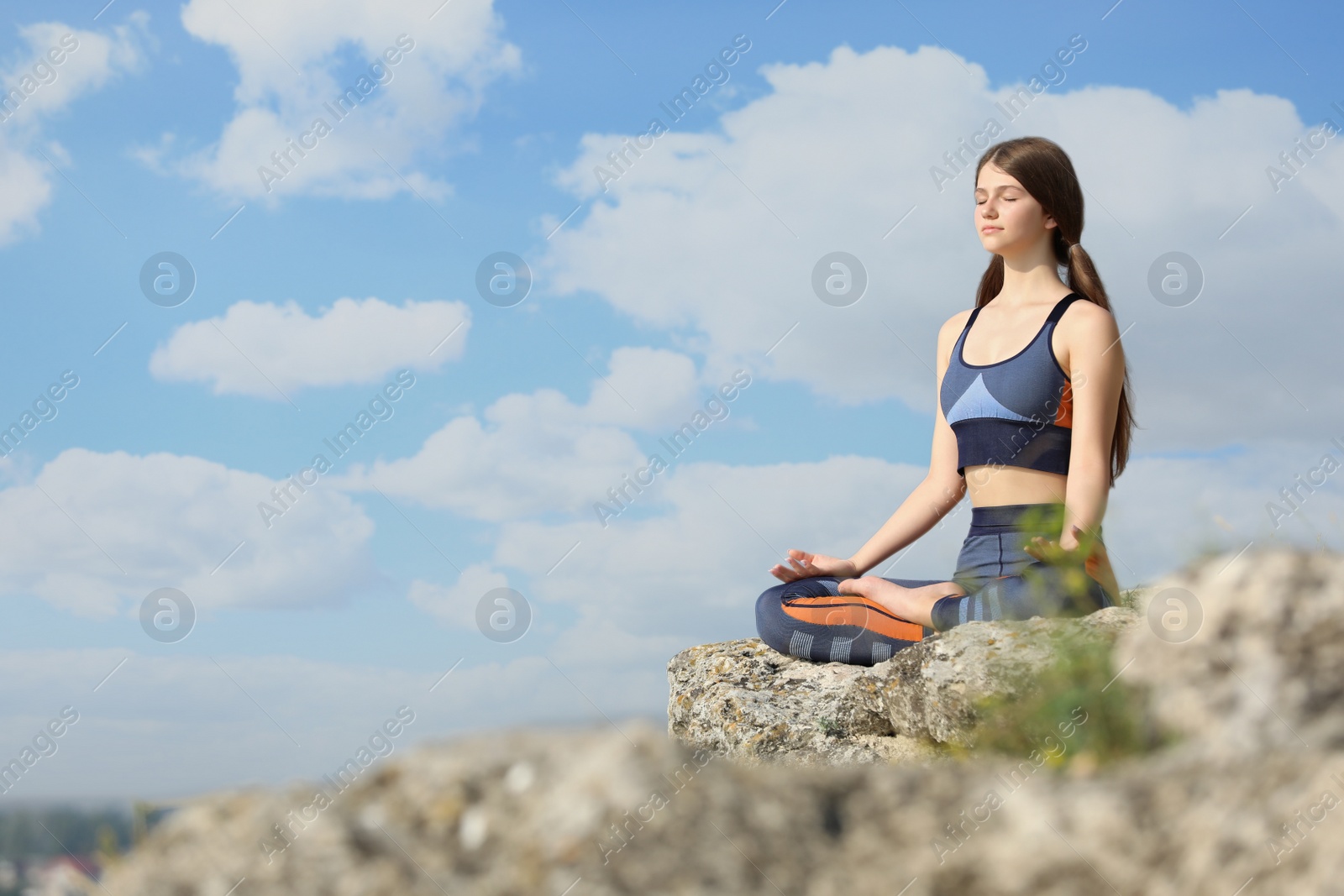 Photo of Teenage girl meditating on cliff. Space for text