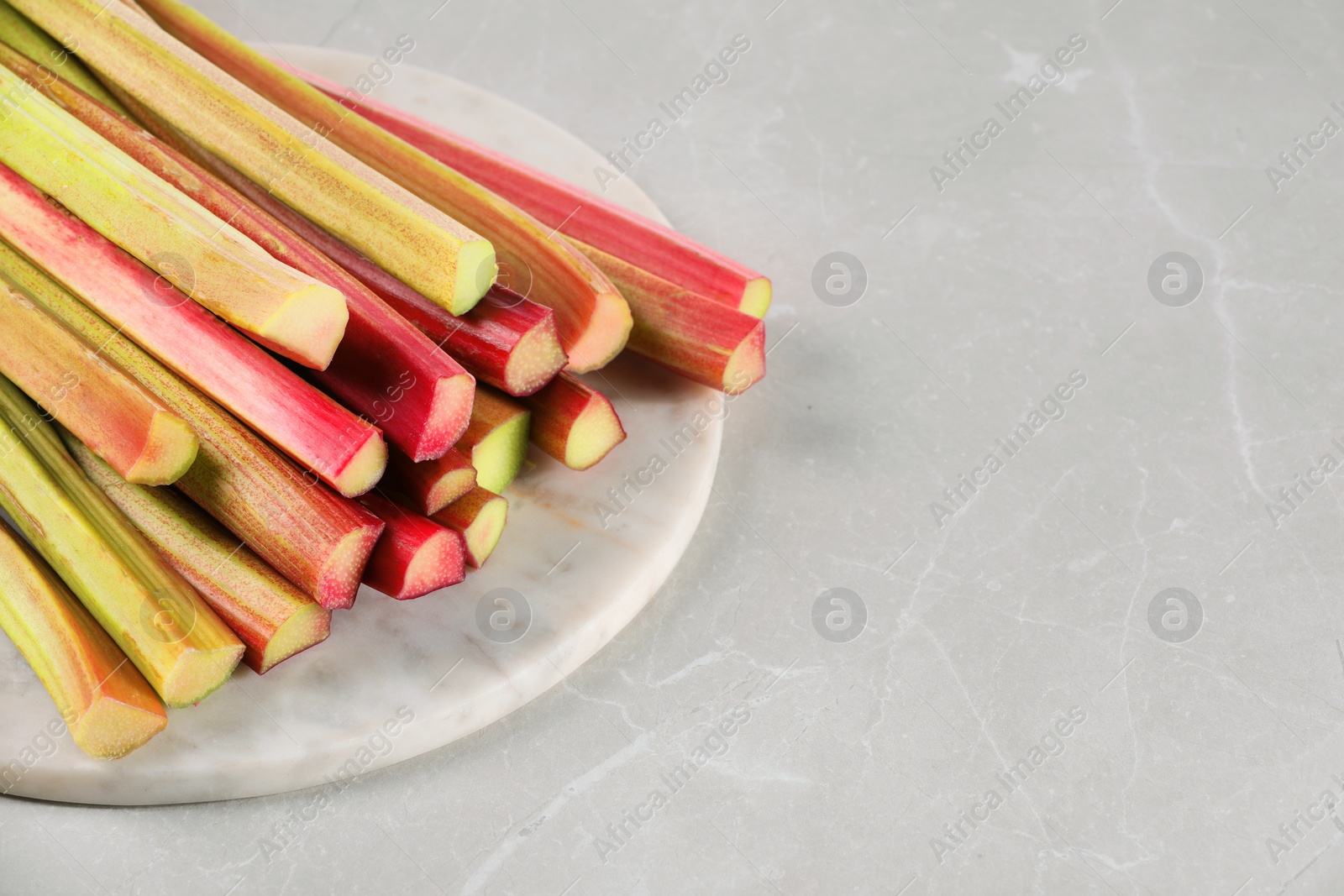 Photo of Fresh ripe rhubarb stalks on light grey table, closeup. Space for text