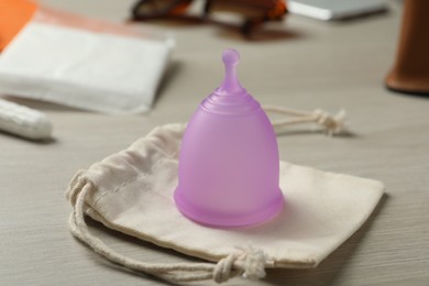 Violet menstrual cup with cotton bag on white wooden table