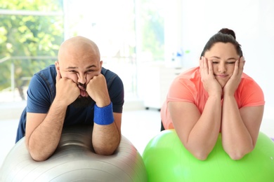 Photo of Tired overweight man and woman resting on fitness balls in gym