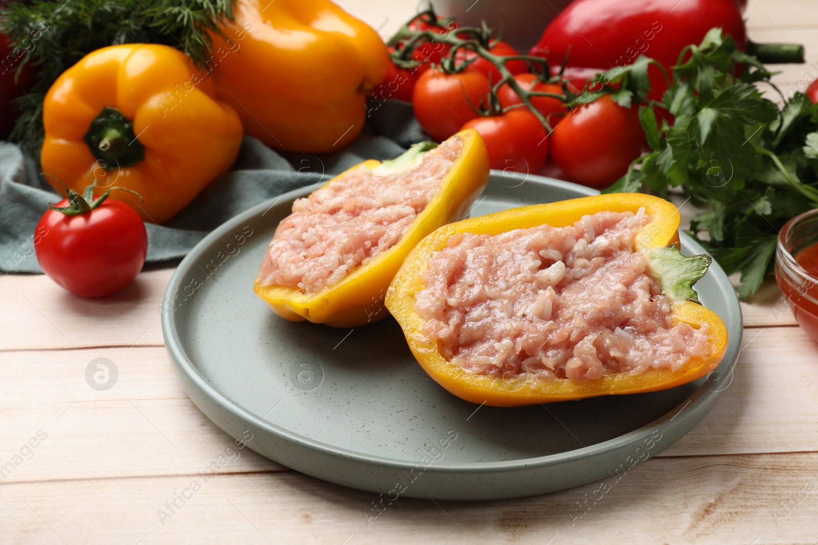 Photo of Raw stuffed peppers with ground meat and ingredients on light wooden table