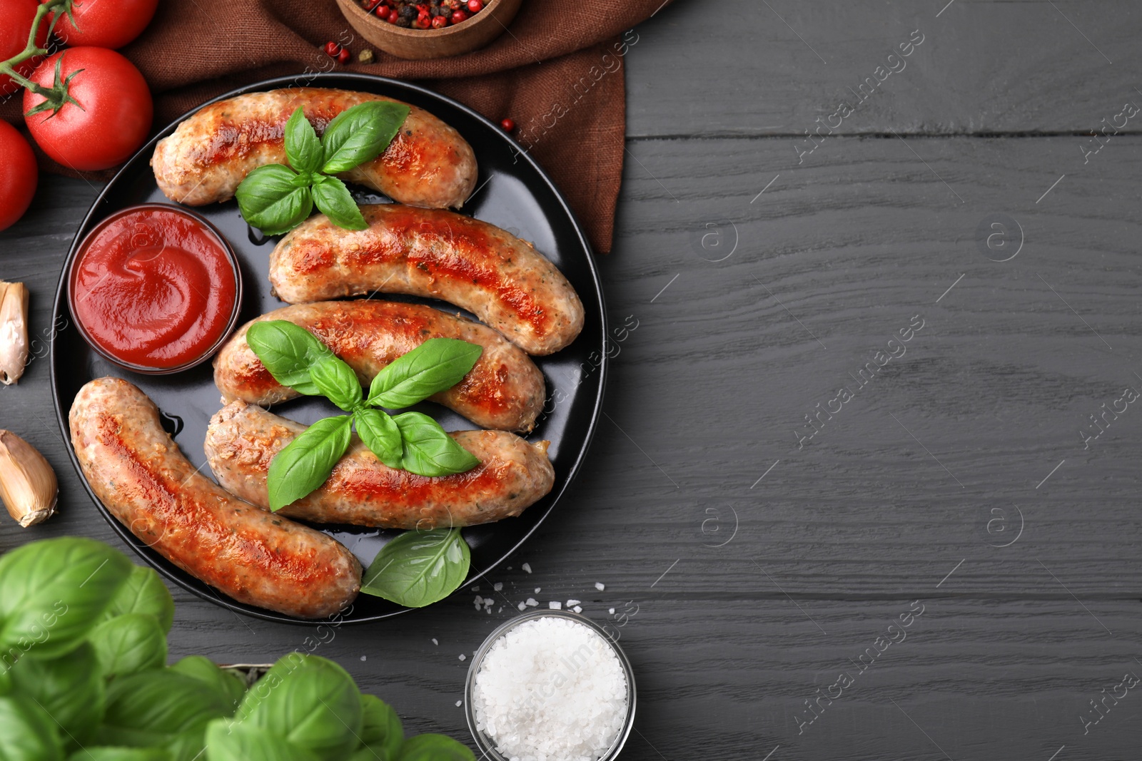 Photo of Tasty homemade sausages served with ketchup and products on grey wooden table, flat lay. Space for text