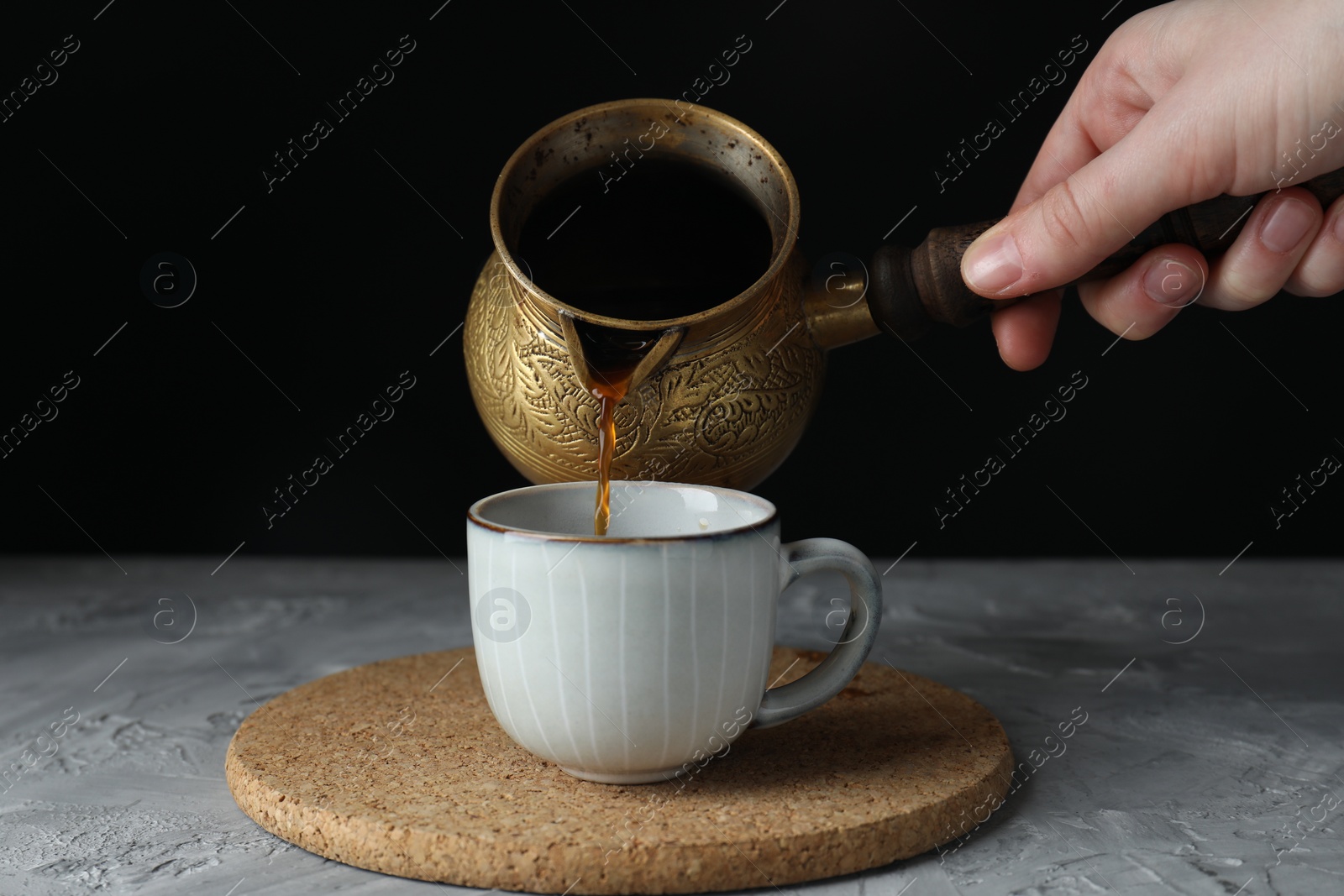 Photo of Turkish coffee. Woman pouring brewed beverage from cezve into cup at grey table, closeup