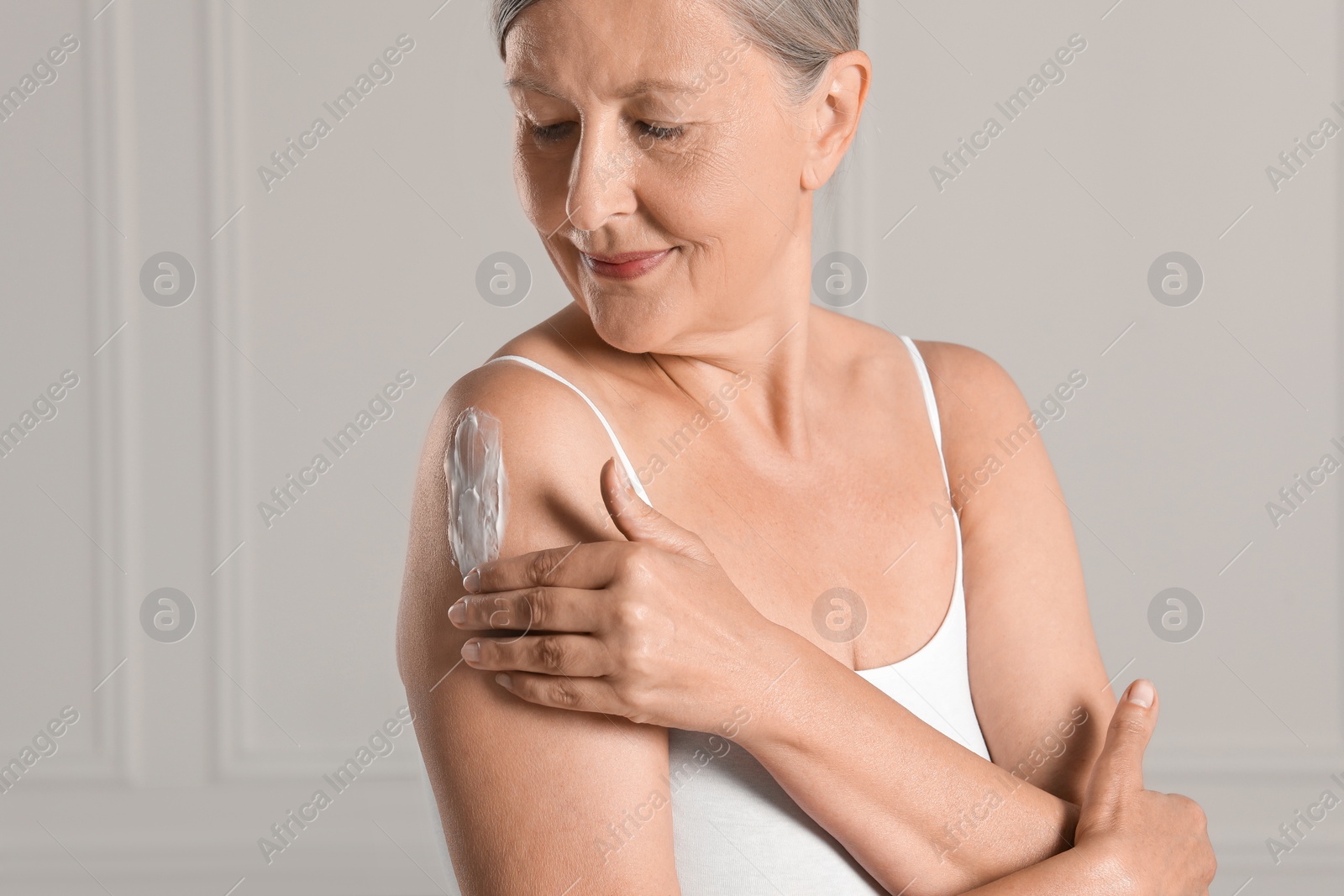 Photo of Happy woman applying body cream onto shoulder near white wall