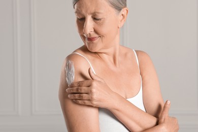 Happy woman applying body cream onto shoulder near white wall