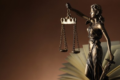 Statue of Lady Justice near book on brown background, space for text. Symbol of fair treatment under law