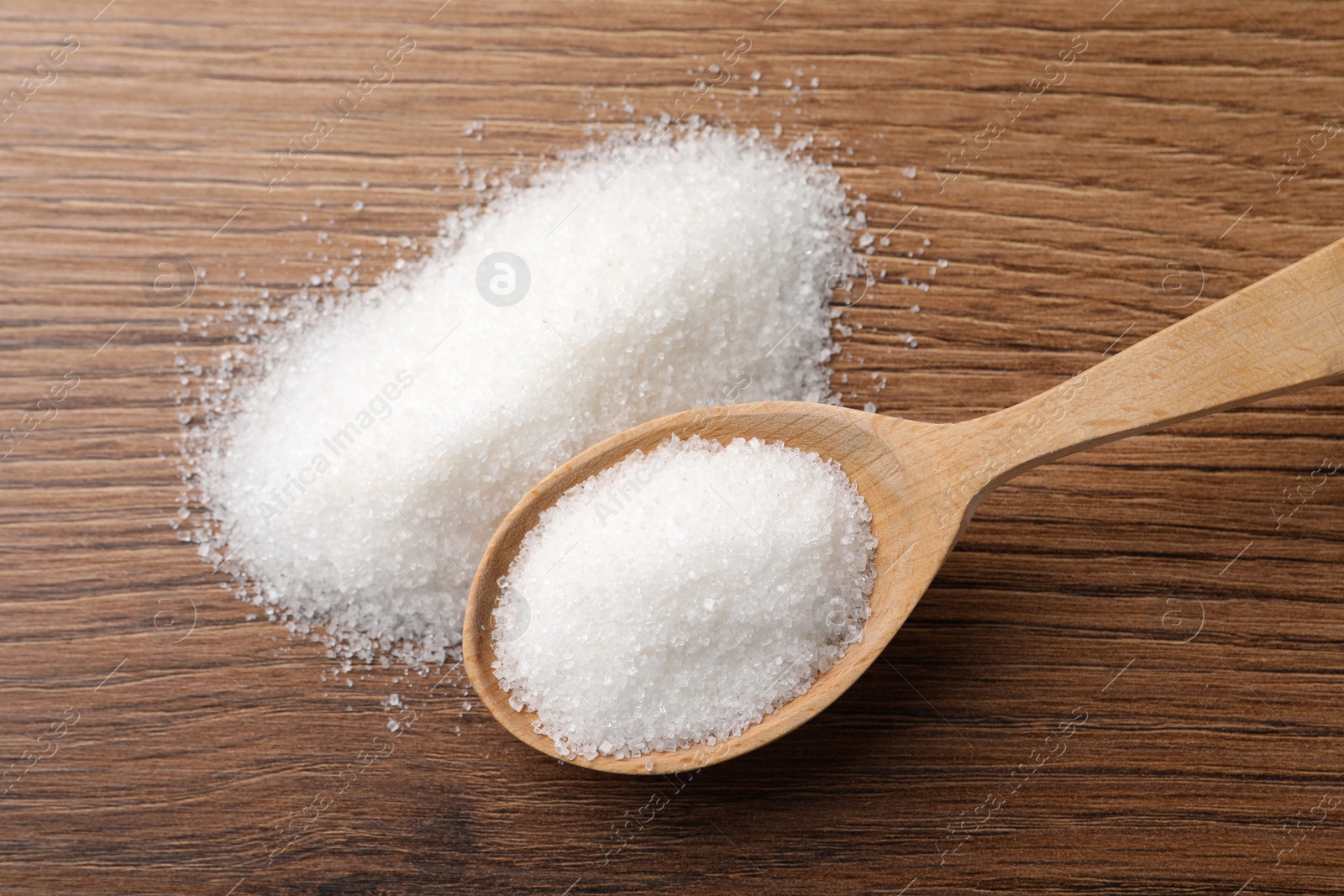 Photo of Granulated sugar and spoon on wooden table, flat lay