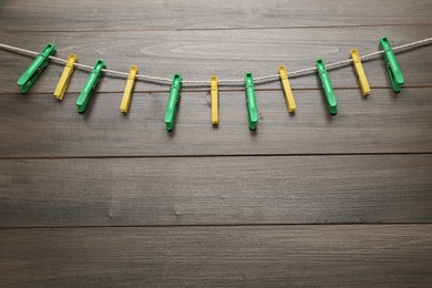 Photo of Colorful plastic clothespins and rope on wooden background. Space for text