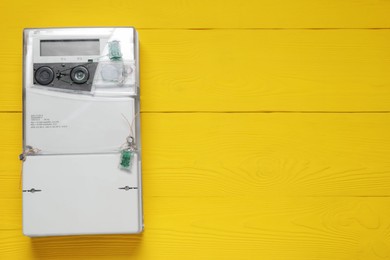 Photo of Electricity meter on yellow wooden wall, space for text