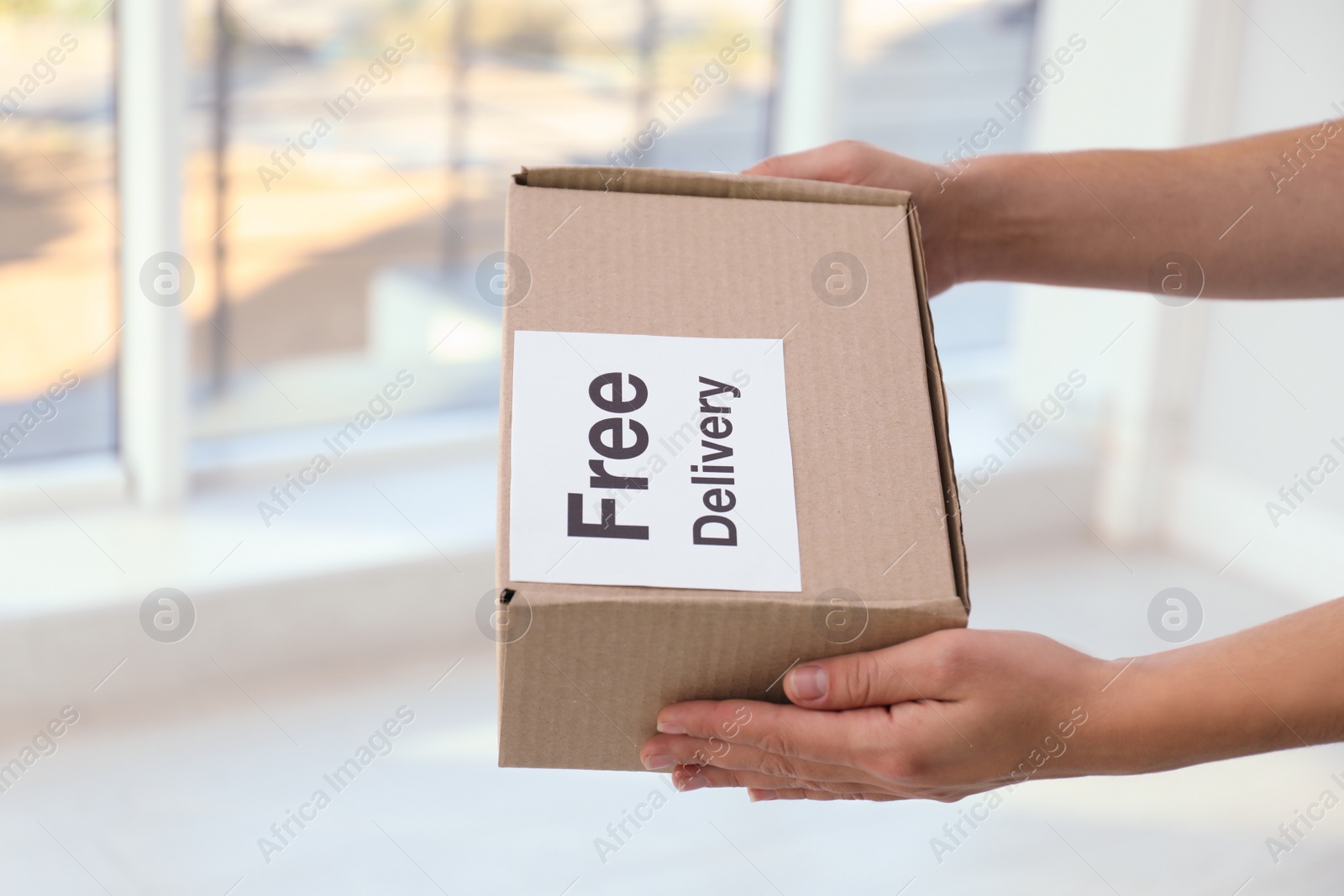 Photo of Courier holding parcel with sticker Free Delivery indoors, closeup