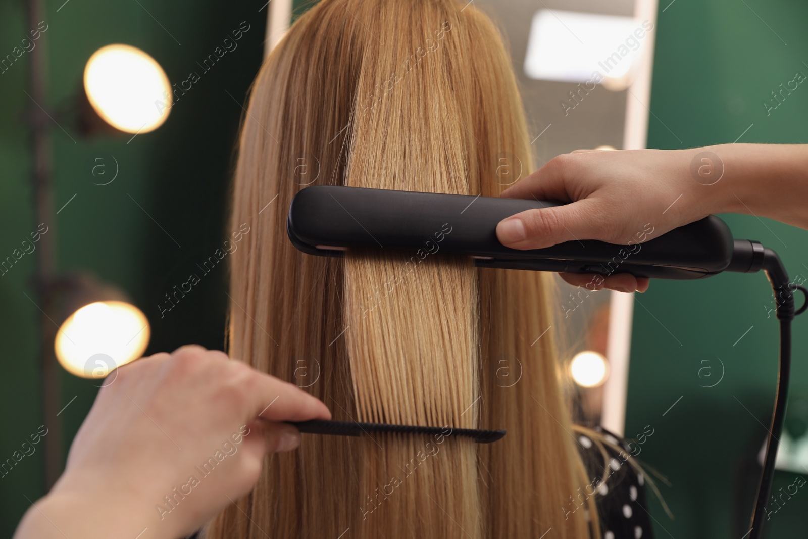 Photo of Stylist straightening woman's hair with flat iron in salon