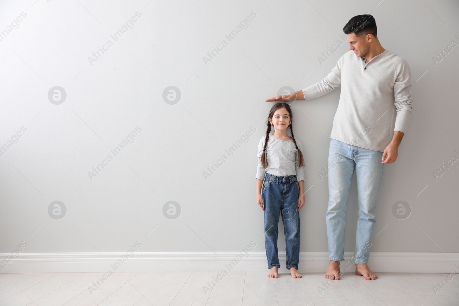 Photo of Father measuring little girl's height near light grey wall indoors. Space for text