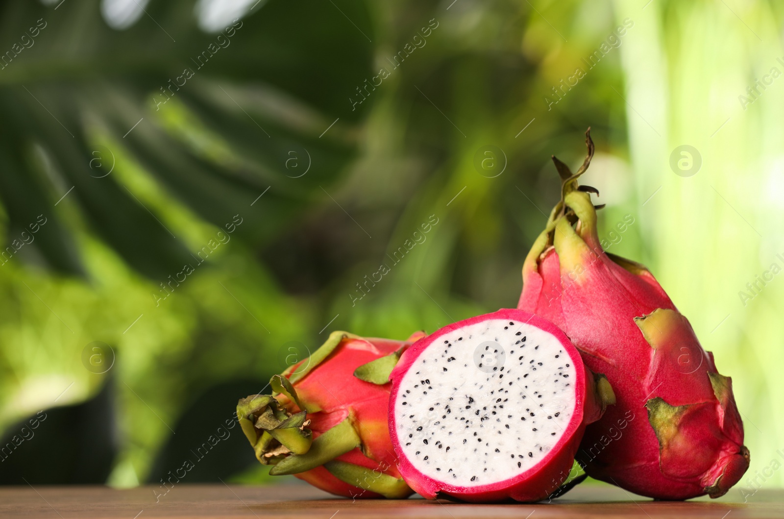 Photo of Delicious cut and whole dragon fruits (pitahaya) on wooden table. Space for text