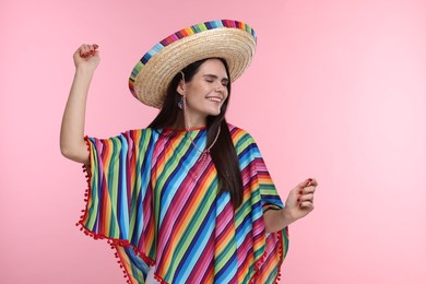 Young woman in Mexican sombrero hat and poncho dancing on pink background. Space for text