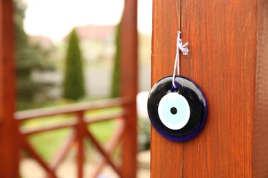 Photo of Evil eye amulet hanging on wooden pillar outdoors, closeup. Space for text