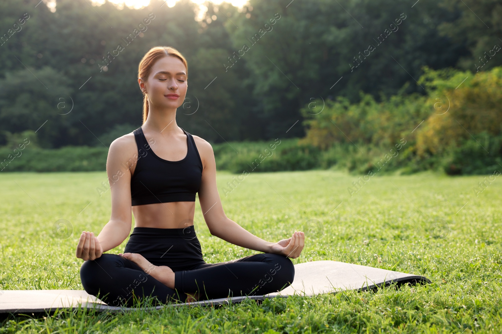 Photo of Beautiful young woman practicing Padmasana on yoga mat outdoors. Lotus pose