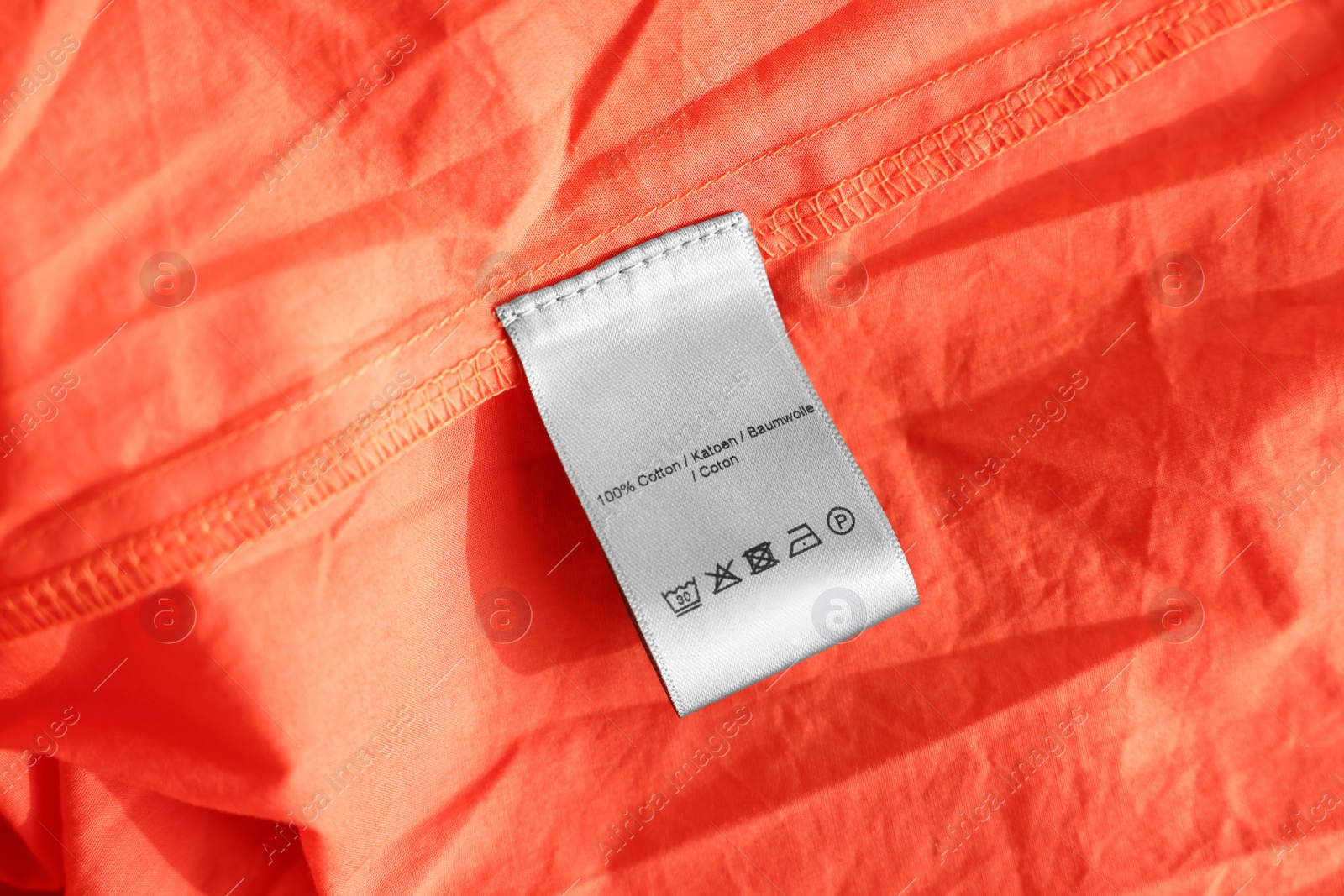 Photo of Clothing label in different languages on orange garment, closeup