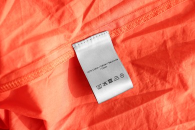 Clothing label in different languages on orange garment, closeup