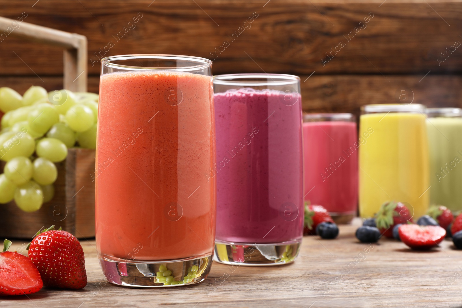 Photo of Glasses with different tasty smoothies and ingredients on wooden table, closeup