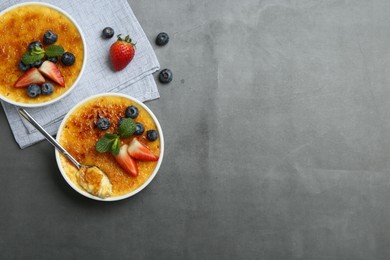 Photo of Delicious creme brulee with berries and mint in bowls on grey table, flat lay. Space for text