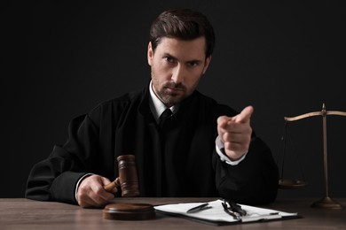 Judge with gavel and papers pointing at wooden table against black background