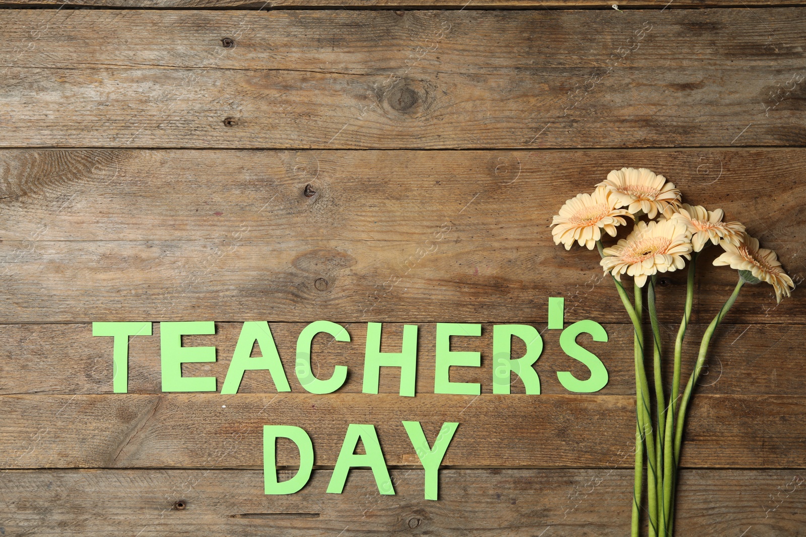 Photo of Words TEACHER'S DAY made of paper letters and beautiful flowers on wooden table, flat lay. Space for text