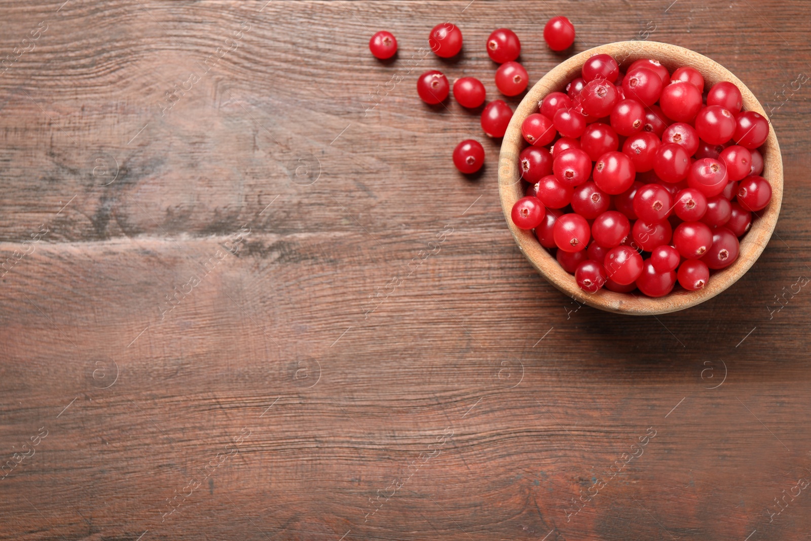 Photo of Tasty ripe cranberries on brown wooden table, flat lay. Space for text