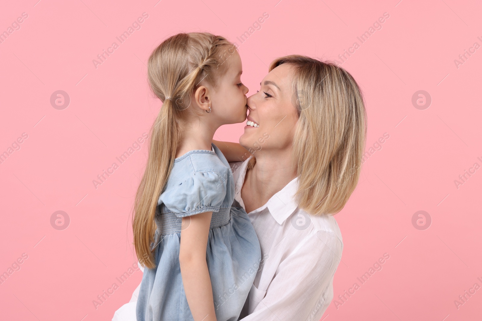 Photo of Daughter kissing her happy mother on pink background