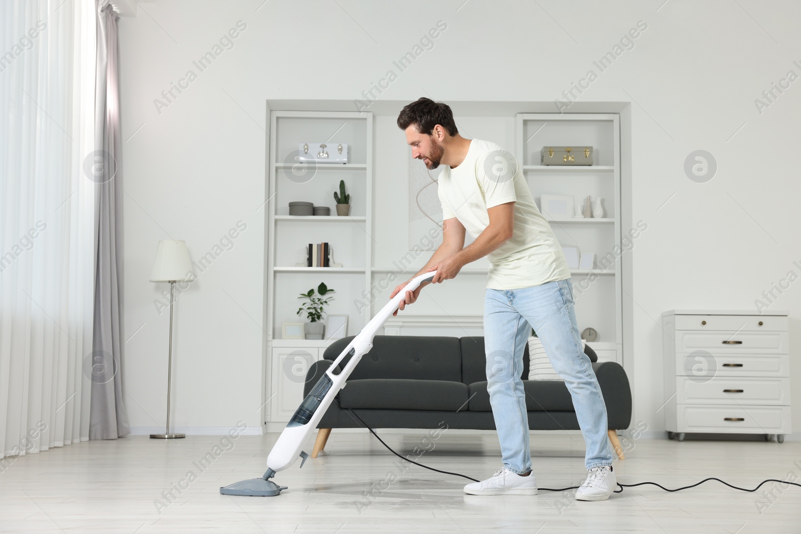 Photo of Happy man cleaning floor with steam mop at home