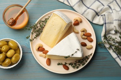 Photo of Tasty Camembert cheese with thyme, honey and nuts on light blue wooden table, flat lay