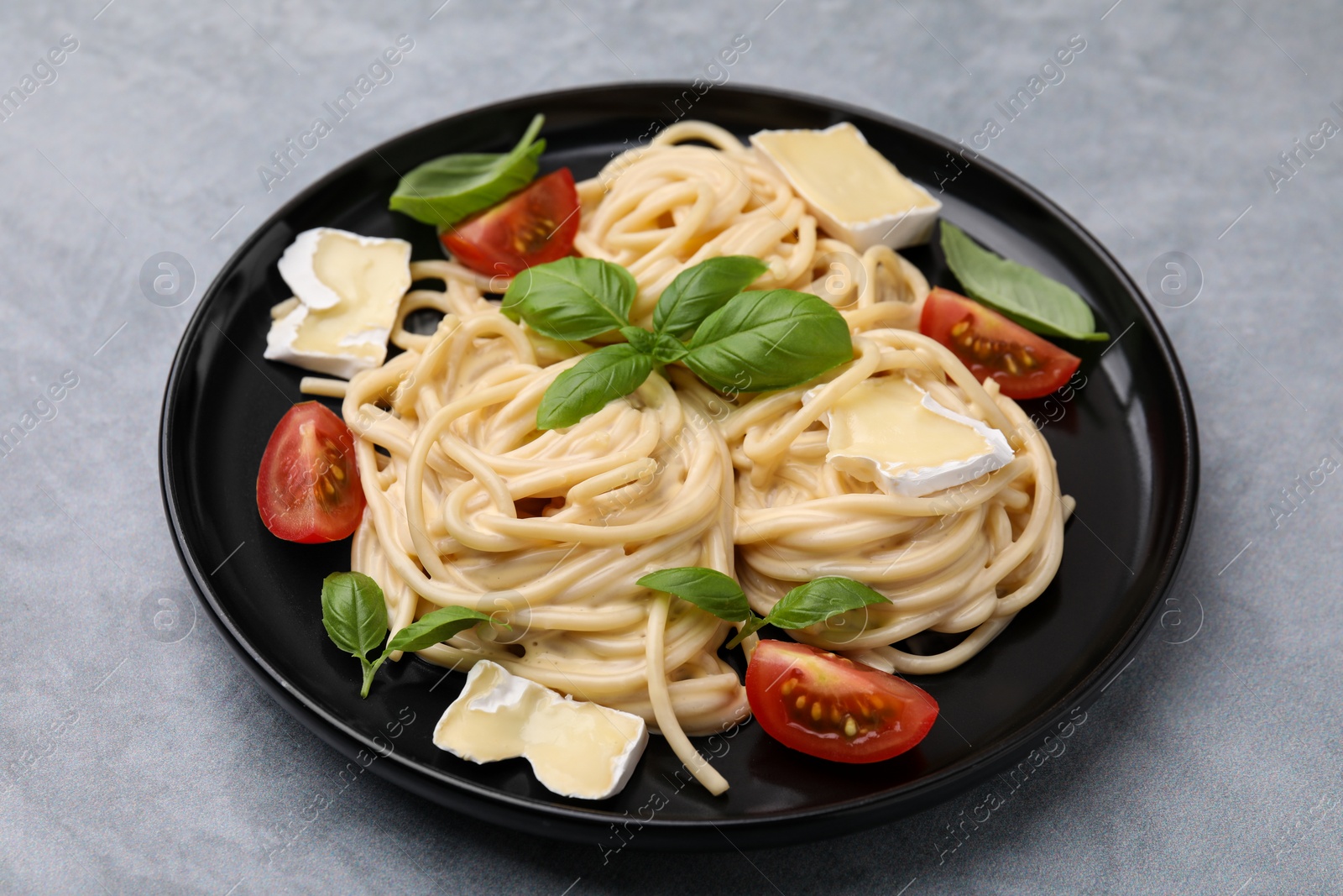 Photo of Delicious pasta with brie cheese, tomatoes and basil leaves on grey table, closeup