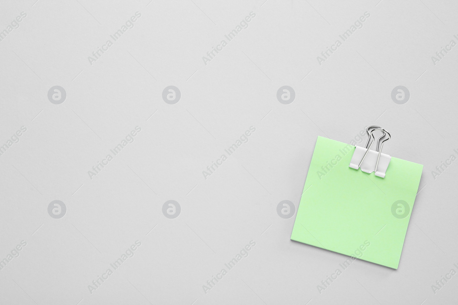 Photo of Blank light green note with white paper clamp on grey background, top view. Space for text