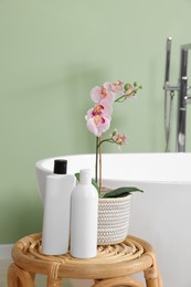 Photo of Stylish ceramic tub, care products and beautiful orchid on coffee table in bathroom