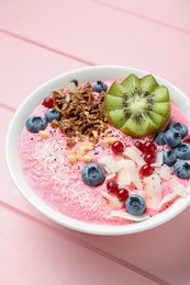 Photo of Tasty smoothie bowl with fresh kiwi fruit, berries and granola on pink wooden table, closeup