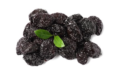 Photo of Heap of sweet dried prunes and green leaves on white background, top view