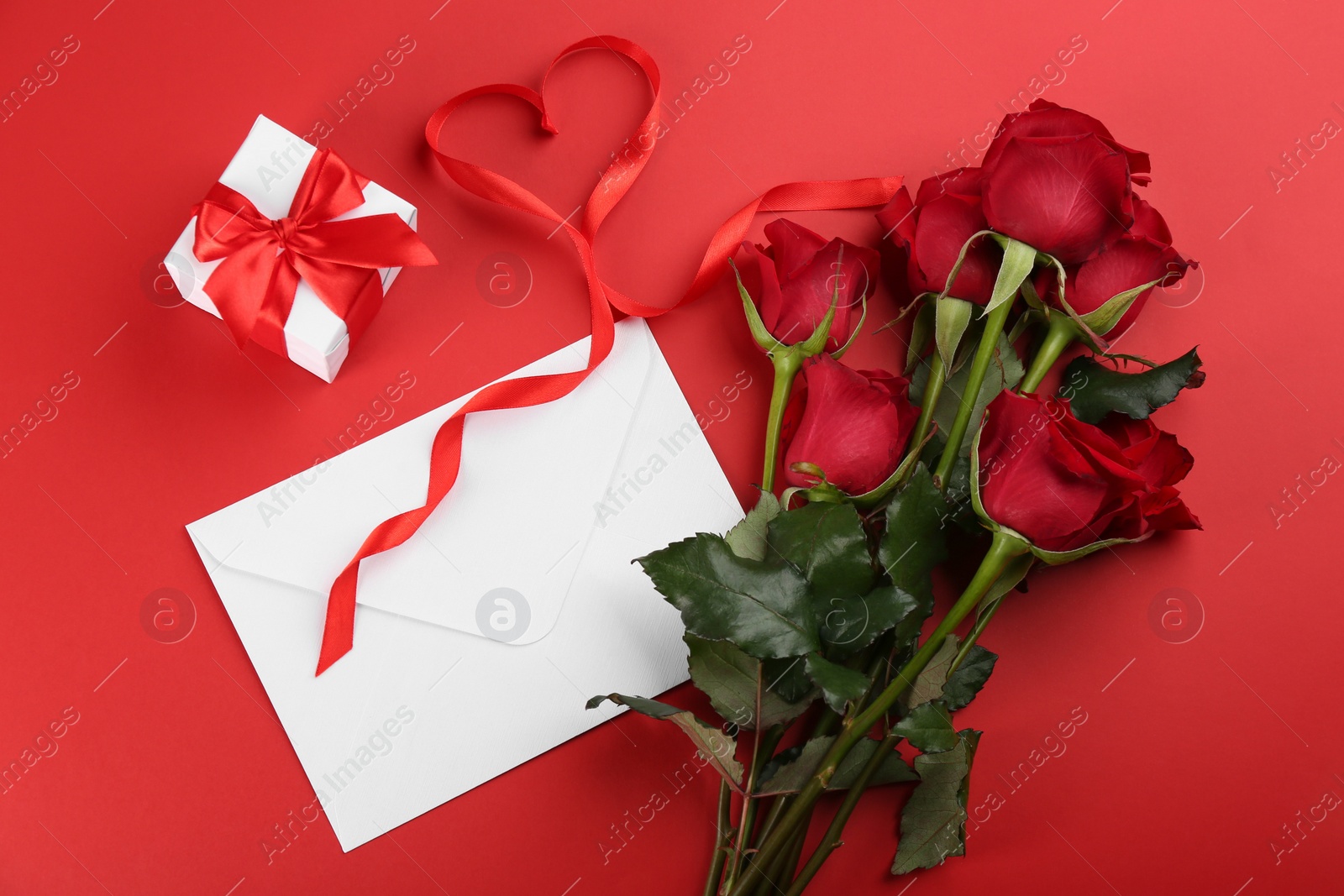 Photo of Flat lay composition with beautiful roses and gift box on red background. Valentine's Day celebration