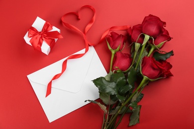 Flat lay composition with beautiful roses and gift box on red background. Valentine's Day celebration