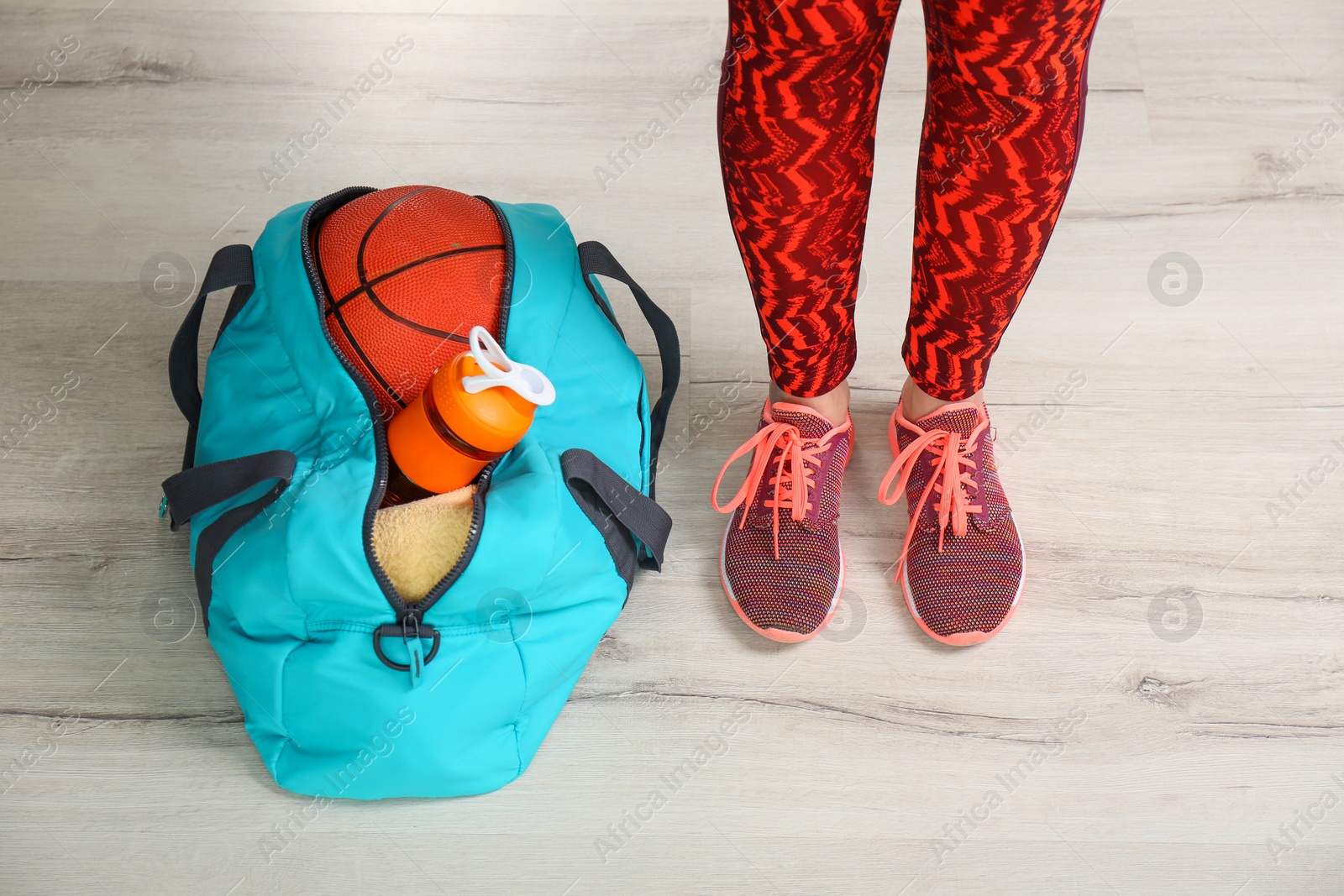 Photo of Young woman in sportswear and bag with gym equipment indoors