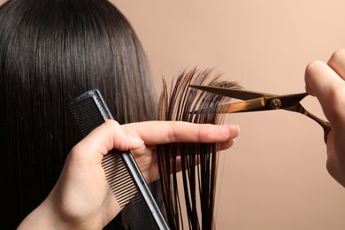 Photo of Hairdresser cutting client's hair with scissors on light brown background, closeup