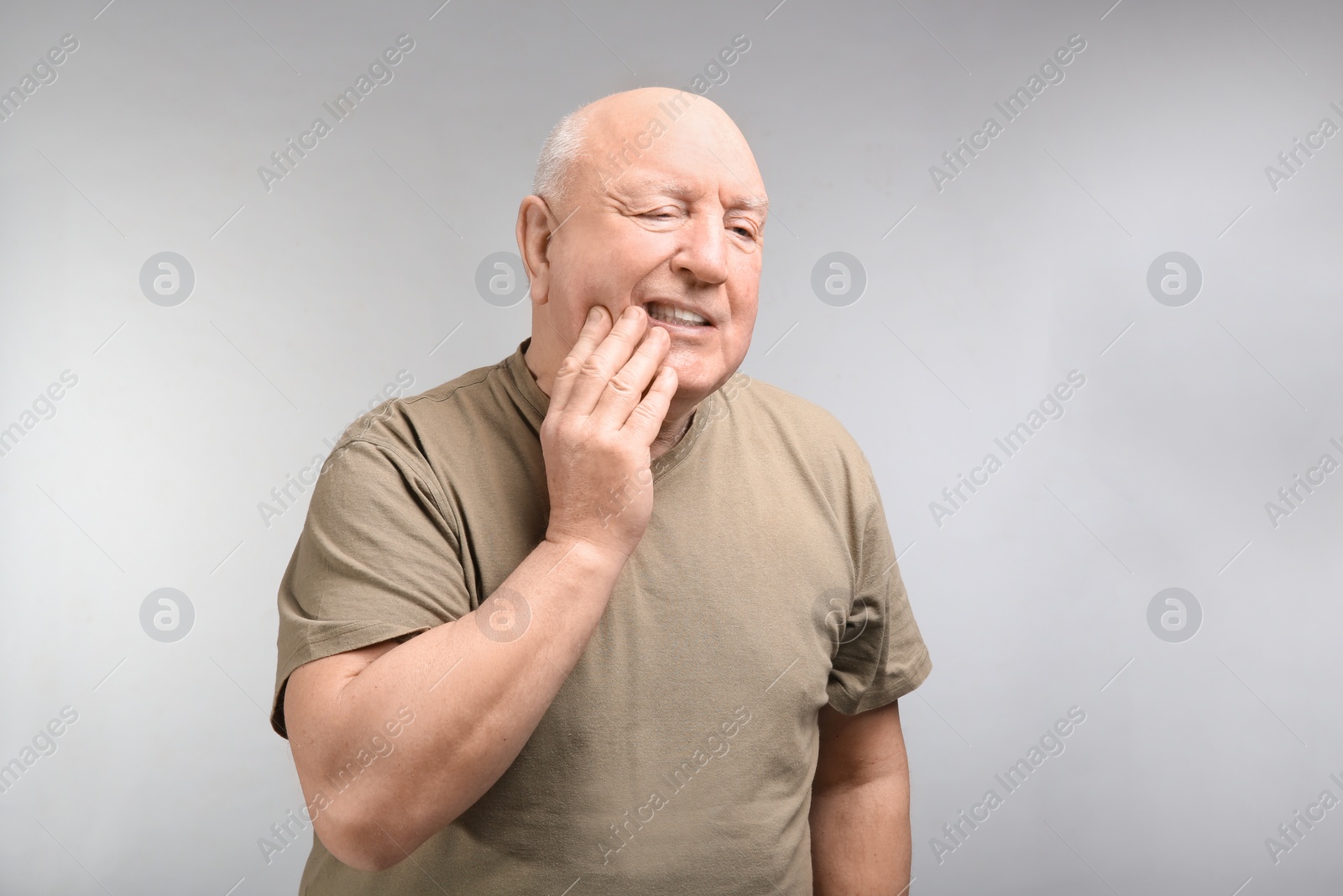 Photo of Senior man suffering from toothache on light background. Enduring pain