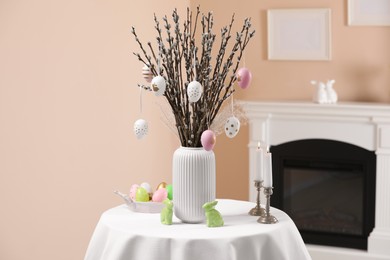 Photo of Pussy willow branches with festively decorated eggs, Easter bunnies and burning candles on table at home