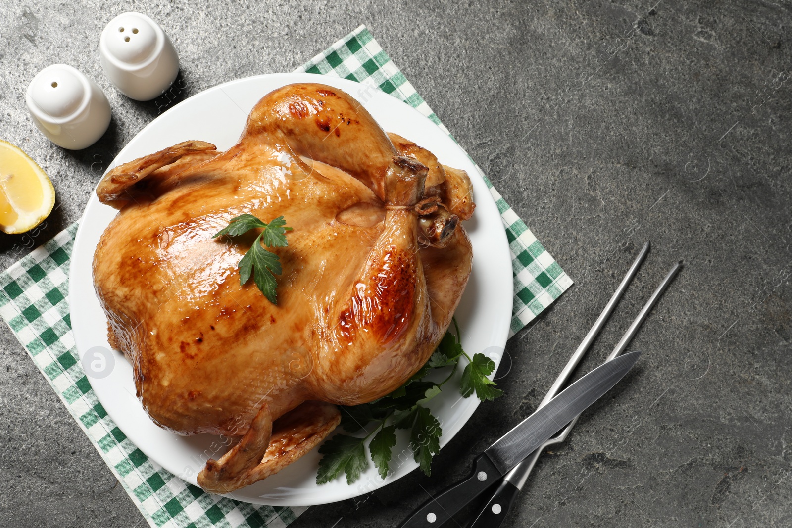 Photo of Tasty roasted chicken with parsley served on grey textured table, flat lay