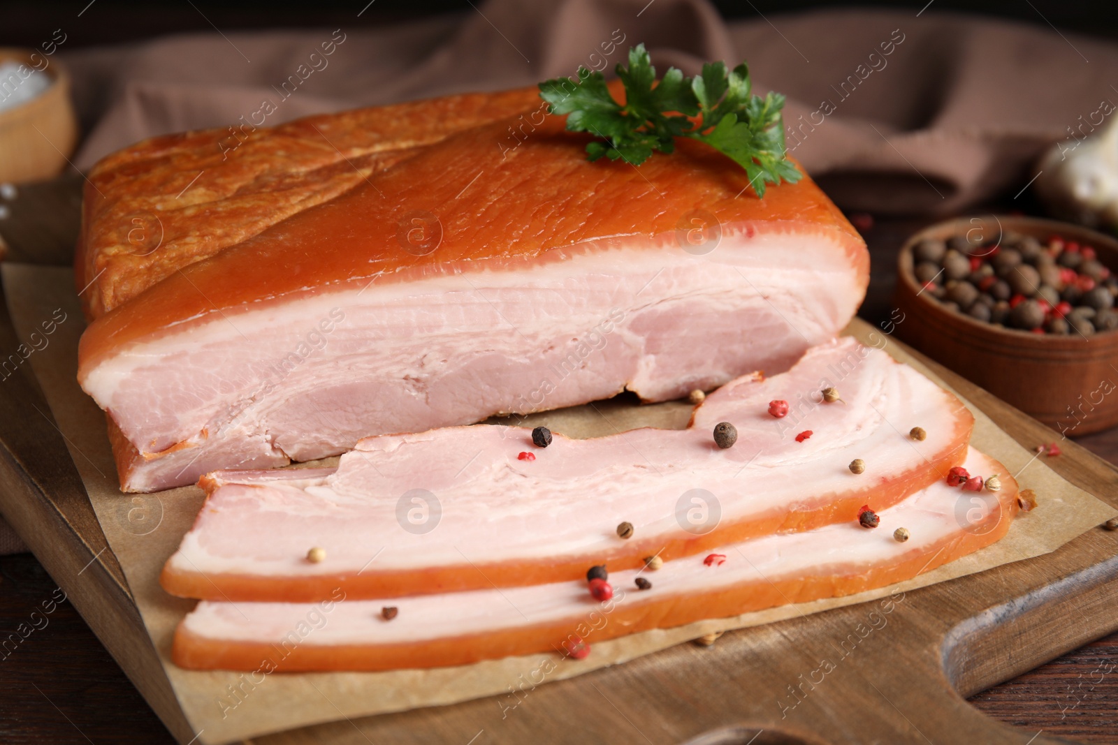 Photo of Delicious smoked bacon with parsley and pepper on wooden board, closeup