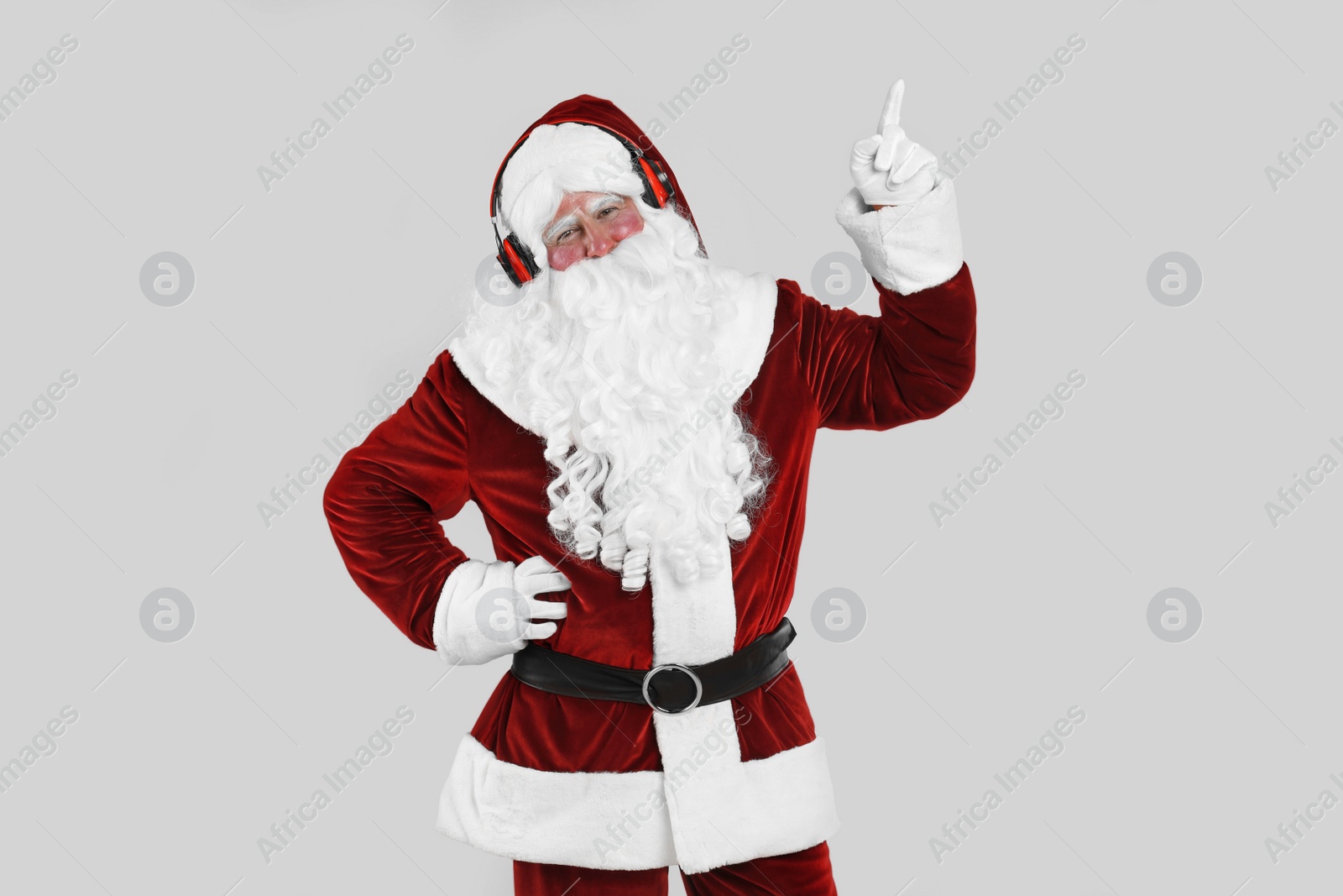 Photo of Santa Claus with headphones listening to Christmas music on light grey background