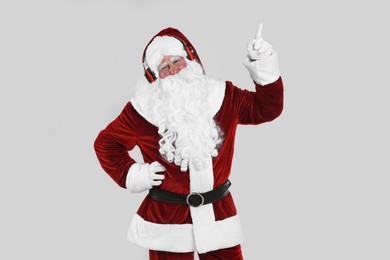 Photo of Santa Claus with headphones listening to Christmas music on light grey background