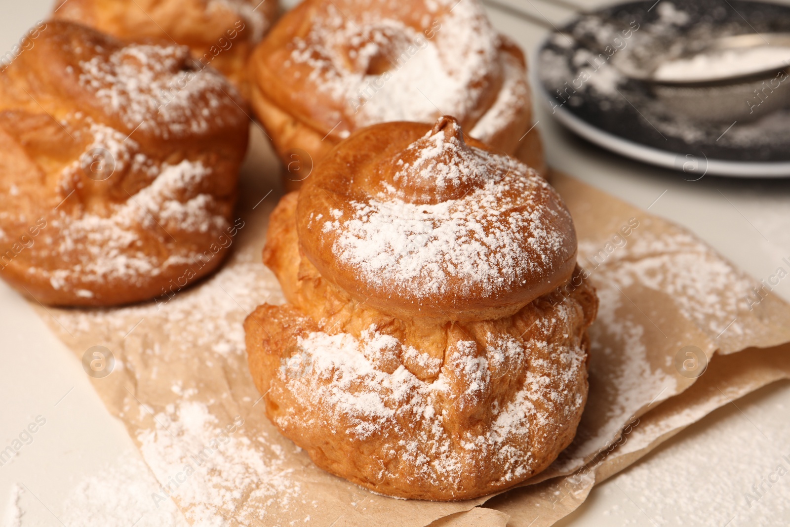 Photo of Delicious profiteroles with powdered sugar on parchment paper, closeup